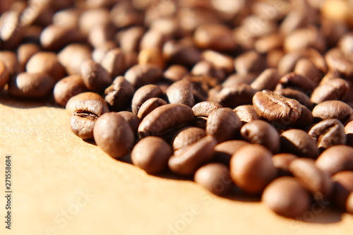 Grains of aromatic roasted coffee scattered on a cardboard surface in the rays of the rising sun.