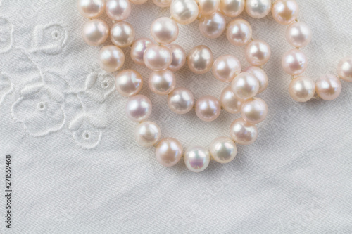 Pearl necklace on white embroidered linen background - top view of string of pink pearls