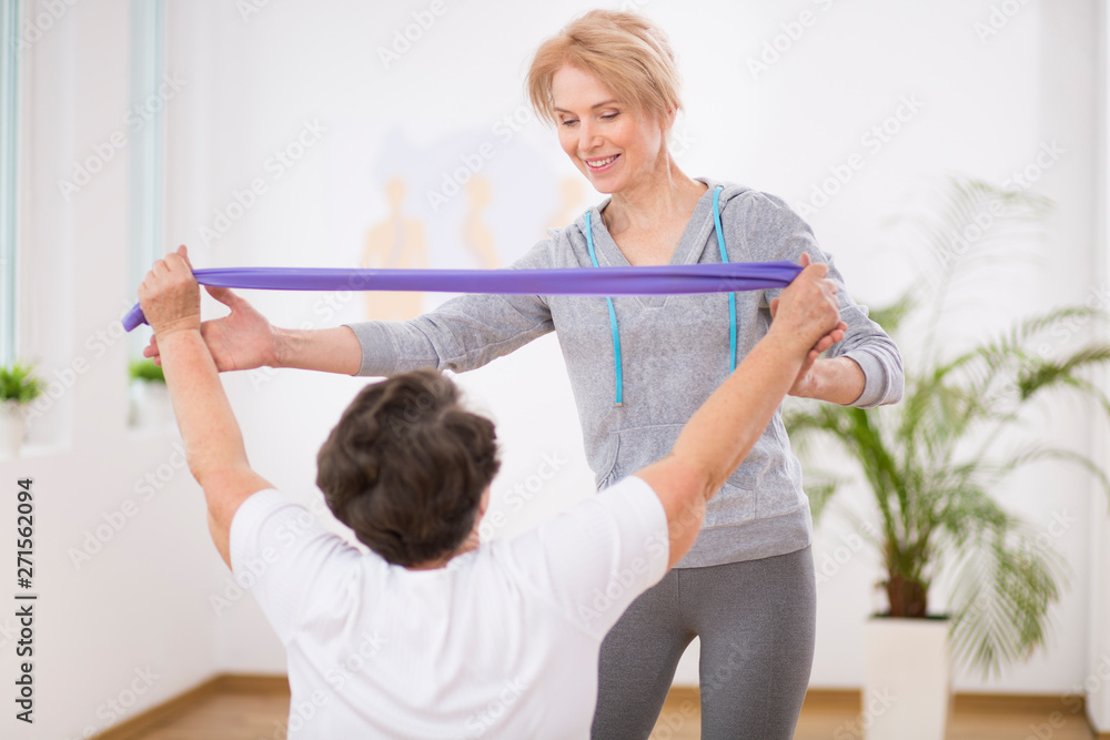 Smiling physiotherapist helping senior woman working out with resistance bands Smiling physiotherapist helping senior woman working out with resistance bands