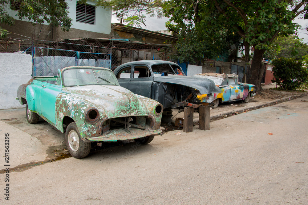 Classic cars under repair in the middle of a street in Havana