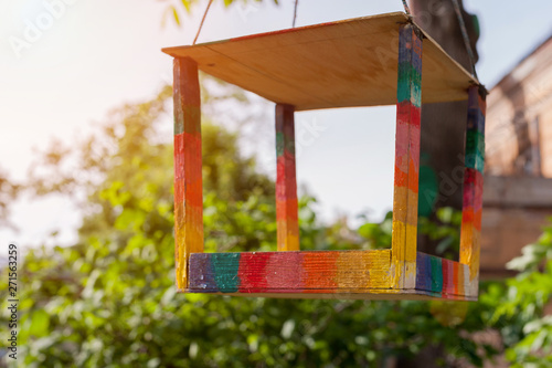 Wooden birdfeeder on tree in rainbow color on green background in sunny day