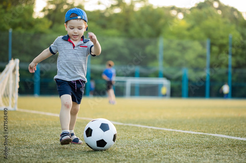 young little kid 3 or 5  years old enjoying happy playing football soccer at grass city park field posing smiling proud standing holding the ball in childhood sport passion and healthy lifestyle