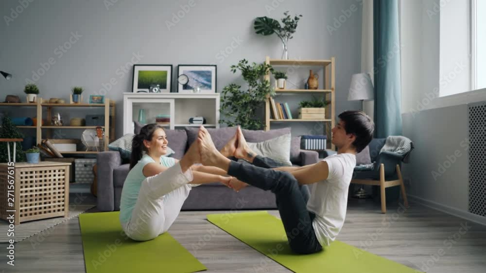 Happy young people exercising at home doing yoga for couples sitting on