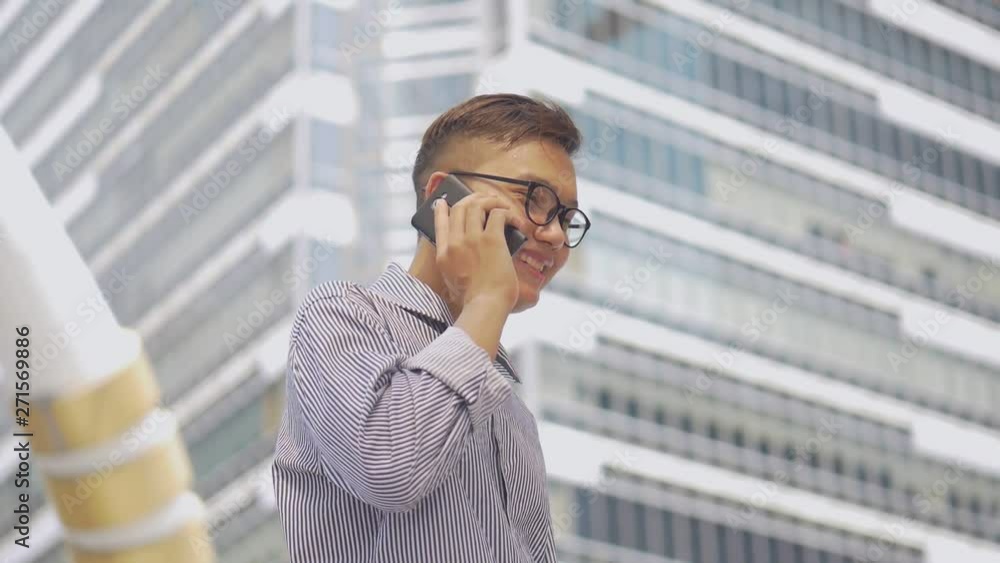 Slow motion portrait asian businessman answers the phone. Asian man with glasses use phone in street near big office building. Slow motion portrait asian businessman answers the phone. Asian man with glasses use phone in street near big office building.