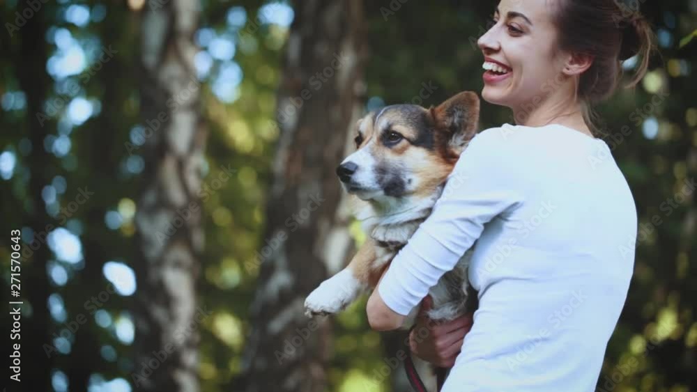 young pretty smiling woman with cute Welsh Corgi dog walking in park. attractive woman standing on the green leaves background with dog, gentle stroking and huging him. Affectionate, gentle and caring young pretty smiling woman with cute Welsh Corgi dog walking in park. attractive woman standing on the green leaves background with dog, gentle stroking and huging him. Affectionate, gentle and caring