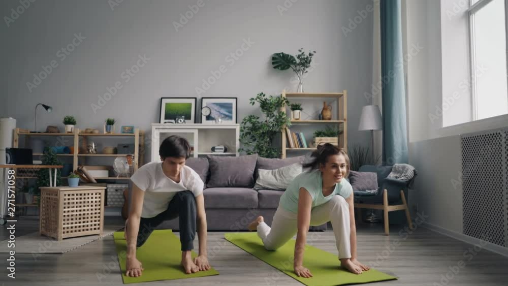 Beautiful couple Caucasian girl and Asian guy are doing yoga at home practising on yoga mats focused on physical exercises. Healthy lifestyle and family concept. Beautiful couple Caucasian girl and Asian guy are doing yoga at home practising on yoga mats focused on physical exercises. Healthy lifestyle and family concept.