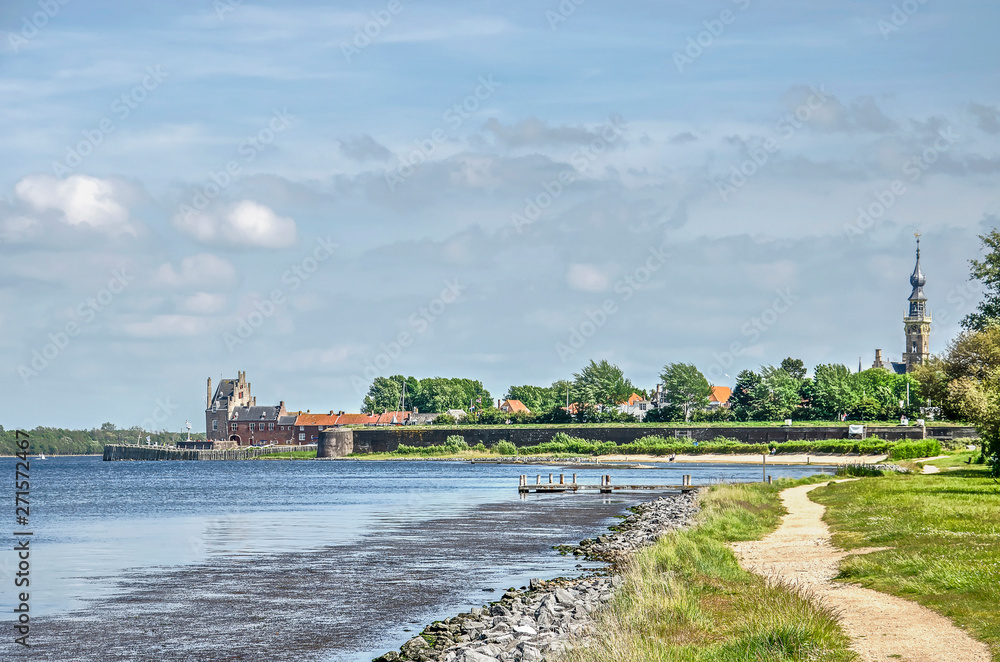 Footpath along the coast of Veersche Meer former estuary towards the town of Veere, The Nethrlands, with its ramparts, fortifications and town hall tower