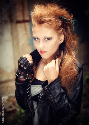 sexy woman model in leather bib and plaid grunge style shirt in ripped mesh pantyhose with blonde hair with Mohawk and smoky bright makeup.holds the collar of the jacket , portrait close-up.