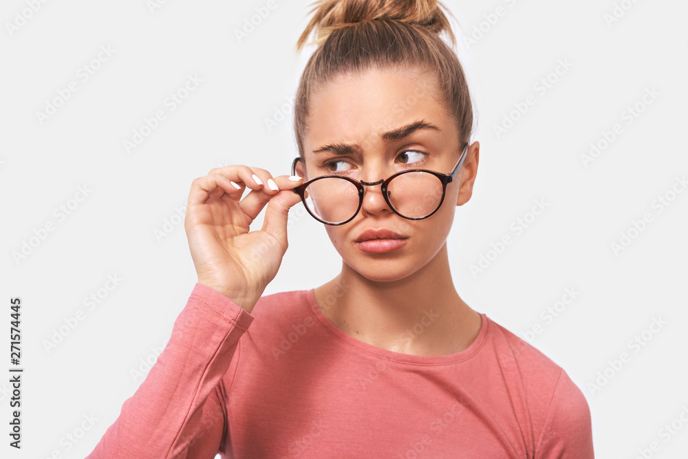 Studio closeup portrait of young woman frowning puzzled faces. Beautiful female woman looking through transparent eyewear at someone aside. People and emotions concept Studio closeup portrait of young woman frowning puzzled faces. Beautiful female woman looking through transparent eyewear at someone aside. People and emotions concept