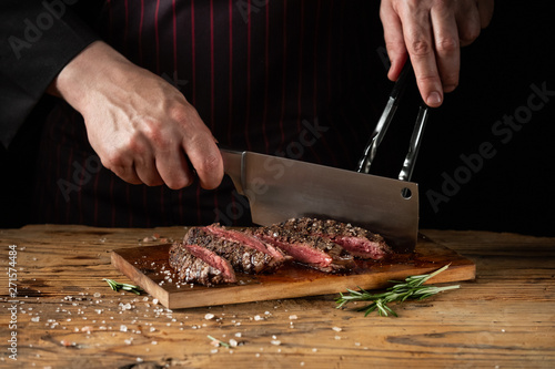 Slicing juicy beef steak by knife in chef hands closeup. Food cooking concept. Dark black background copy space.