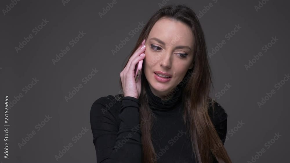 Portrait of attractive brunette woman talking on cellphone being glad and positive isolated on gray background. Portrait of attractive brunette woman talking on cellphone being glad and positive isolated on gray background.