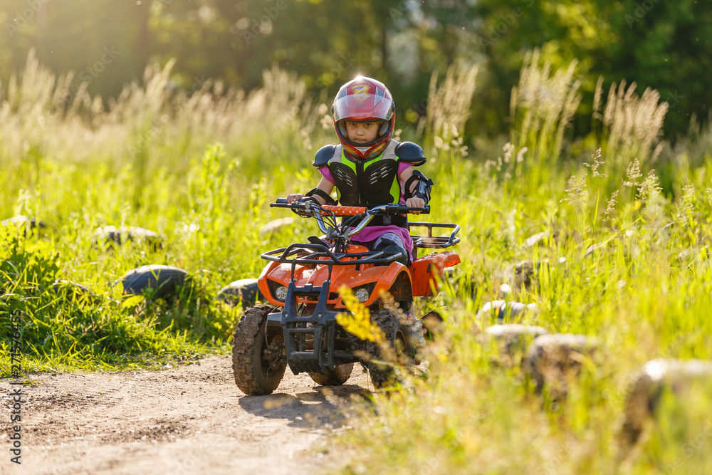 The little girl rides a quad bike. A mini quad bike is a cool girl