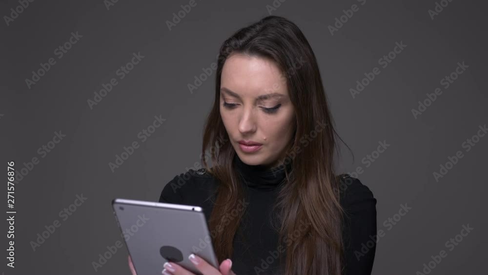 Portrait of attractive brunette woman working with tablet being attentive and concentrated isolated on gray background. Portrait of attractive brunette woman working with tablet being attentive and concentrated isolated on gray background.