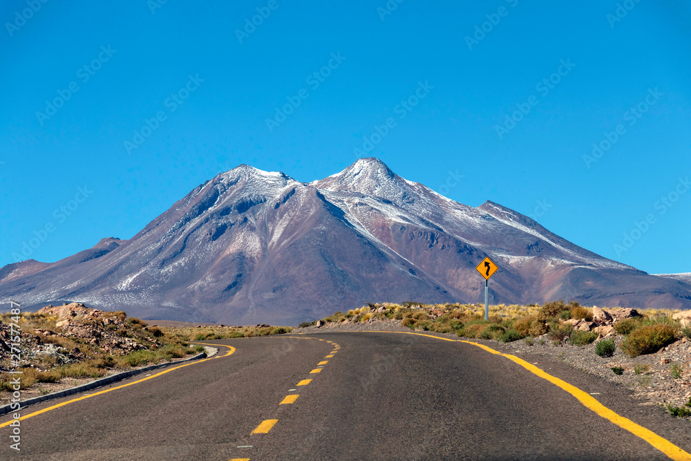 Desert road curve in Atacama: yellow sign and barren landscape of desert Desert road curve in Atacama: yellow sign and barren landscape of desert