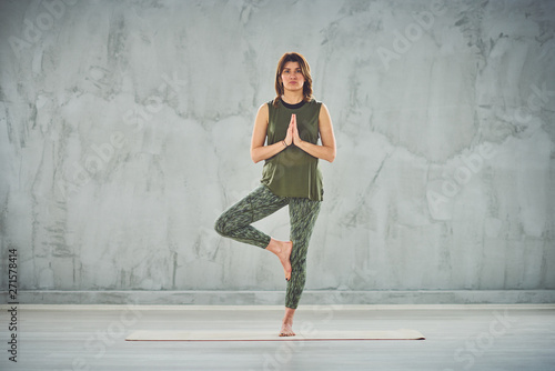 Charming brunette standing on the mat in half lotus pose.