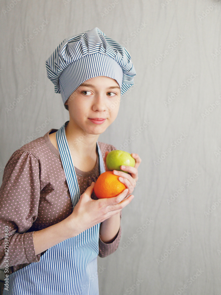 Teen girl in a cook costume holds fruit in hand: green apple and orange. Teen girl in a cook costume holds fruit in hand: green apple and orange.