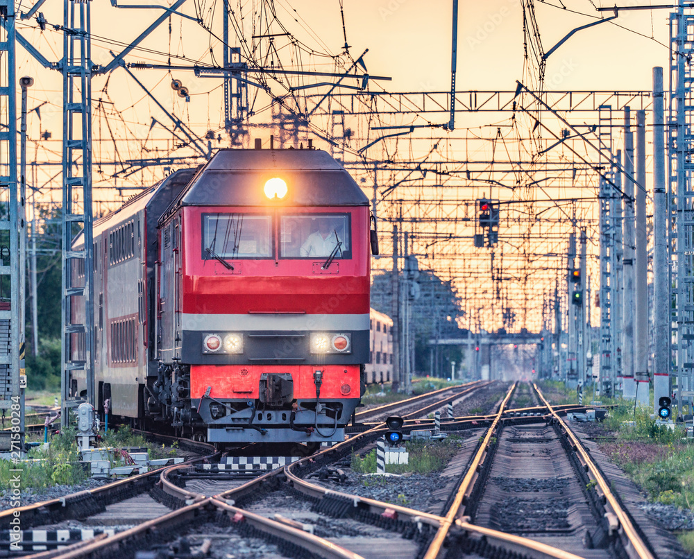 Passenger train departs from the station at sunset time.