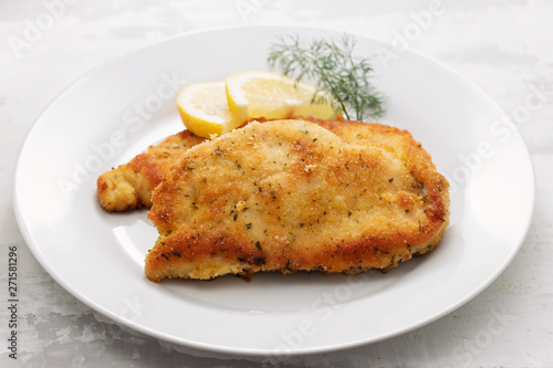 fried chicken with lemon on white plate on ceramic background