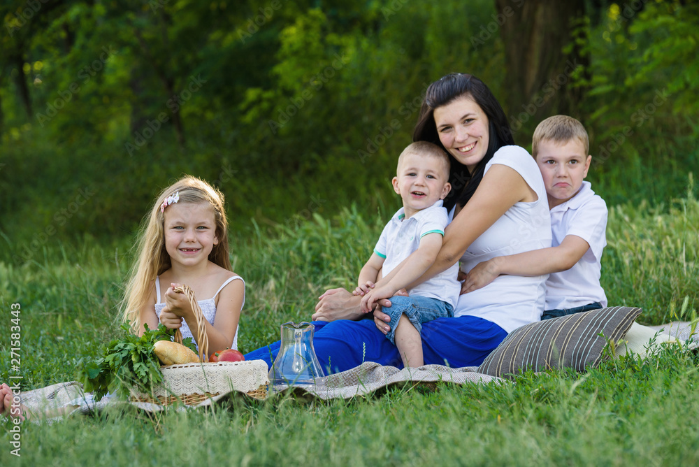 Fototapeta premium Happy woman with her three kids sits on the plaid outdoor. Family picnic