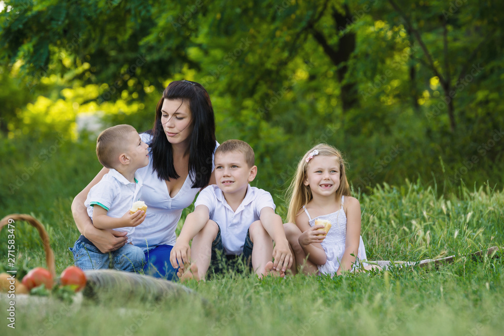 Naklejka premium Happy woman with her three kids sits on the plaid outdoor. Family picnic