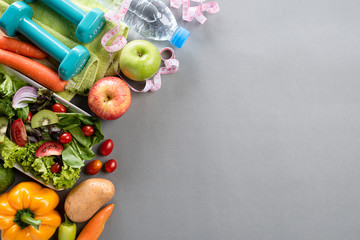 Healthy lifestyle, food and sport concept. Top view of athlete's equipment Weight Scale measuring tape green dumbbell, sport water bottles, fruit and vegetables on gray background.
