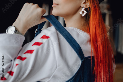 Beautiful Woman Fashion Garment Store Closeup. Epatage Caucasian Redhead Fitting on Trendy Denim Vest. Young Elegant Girl Wearing Massive Earring and Watch. Female Clothes Designer Portrait