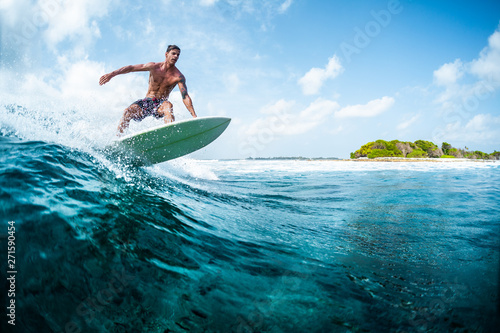 Young surfer with lean muscular body rides the tropical wave
