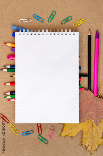 notebook blank page colorful pencil, pen, markers and autumn leaves mock-up composition Back to school concept with stationery office supplies on a brown craft paper background copy space top view