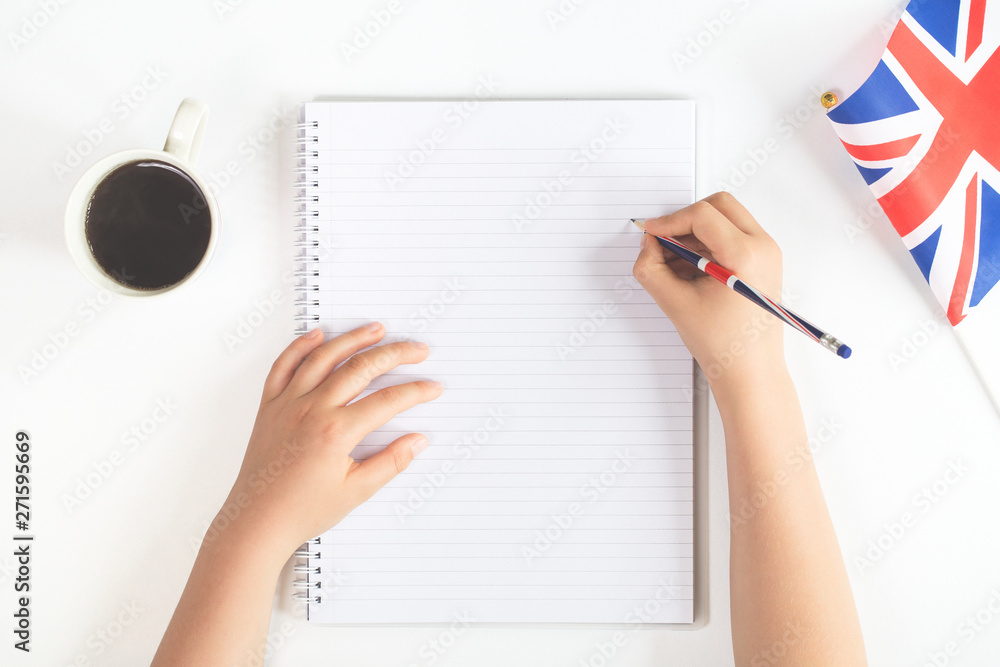 Hands on a desk with a pencil and a blank notebook and british UK English union jack flag and coffee mug. Flat lay with copy space. Education study or English language test learning concept Hands on a desk with a pencil and a blank notebook and british UK English union jack flag and coffee mug. Flat lay with copy space. Education study or English language test learning concept