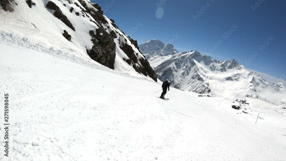 A wide angle male skier aged in black equipment and white helmet with ski poles rides on a snowy slope on a sunny day. The concept of winter ski sports A wide angle male skier aged in black equipment and white helmet with ski poles rides on a snowy slope on a sunny day. The concept of winter ski sports