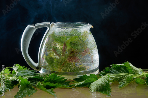 Tea teapot of medicinal nettle with nettle leaves and smoke on a black background photo