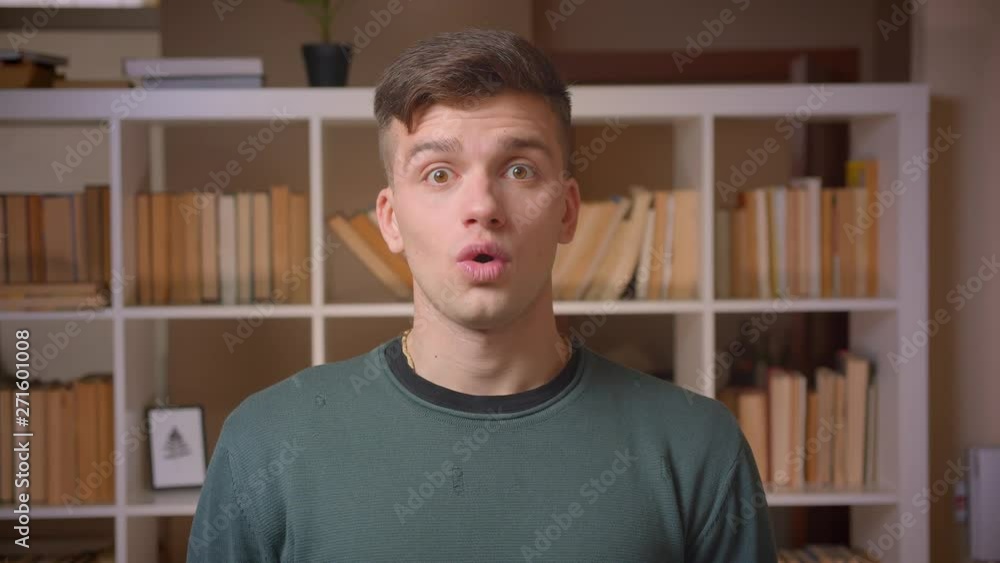 Portrait of young male student shows strong amusement into camera in library. Portrait of young male student shows strong amusement into camera in library.