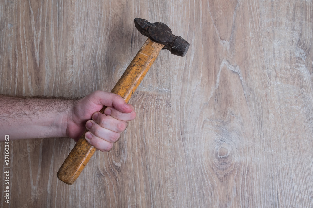 Hammer studio image. Male hand holding a hammer. Hammer tool on blurred wooden background.