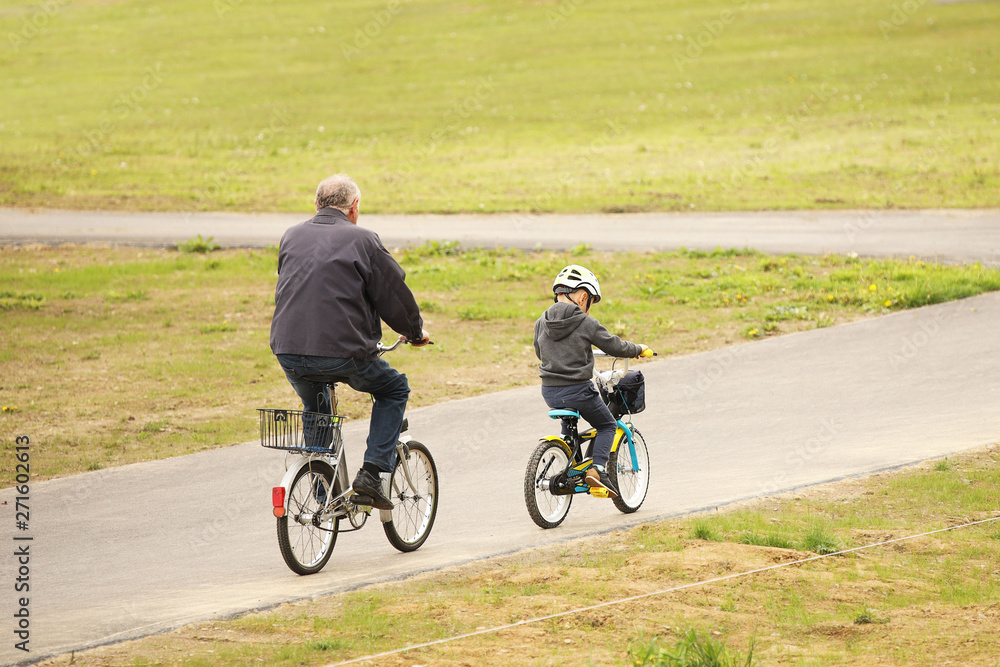 Grandfather and grandson ride bicycles on the asphalt path of the park. Raising the younger generation. Activity of the elderly and children in nature. Sport for a healthy lifestyle. Joyful childhood. Grandfather and grandson ride bicycles on the asphalt path of the park. Raising the younger generation. Activity of the elderly and children in nature. Sport for a healthy lifestyle. Joyful childhood.