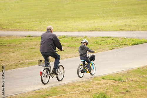 Grandfather and grandson ride bicycles on the asphalt path of the park. Raising the younger generation. Activity of the elderly and children in nature. Sport for a healthy lifestyle. Joyful childhood.