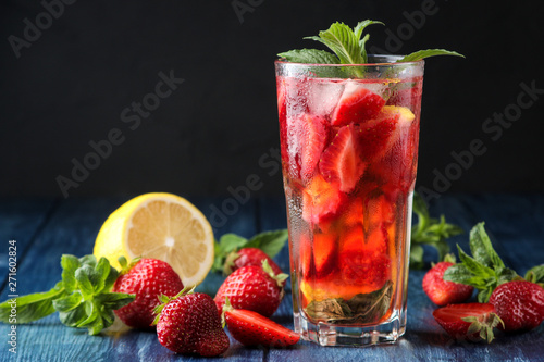 Strawberry Mojito. Cold summer mojito cocktail with strawberries, mint, lemon and ice in a glass on a blue wooden table. on a dark background