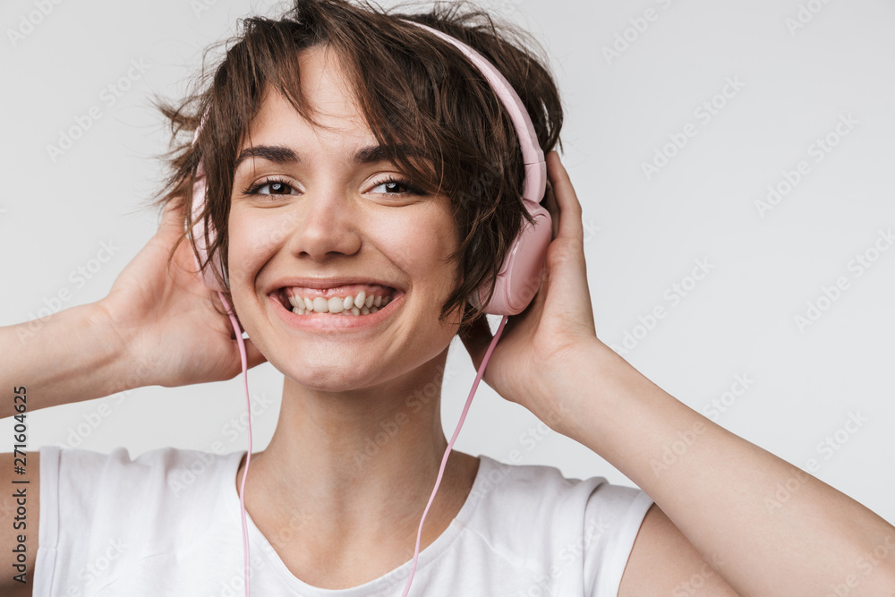 Pretty excited happy woman posing isolated over white wall background listening music with headphones. Pretty excited happy woman posing isolated over white wall background listening music with headphones.