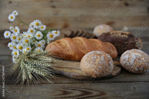 rye and wheat fresh hot bread with ears and a bouquet of daisies on a wooden rustic background, close-up. With copy space for text.