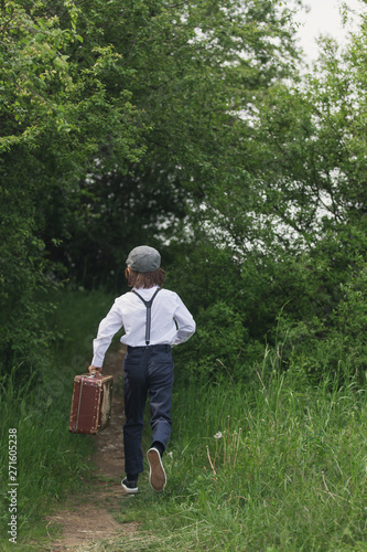 Sweet children in vintage clothing, holding suitcase, running in the park