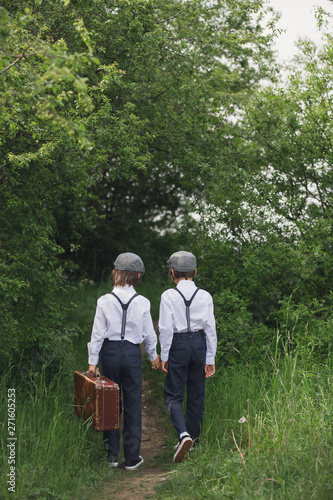 Sweet children in vintage clothing, holding suitcase, running in the park © Tomsickova