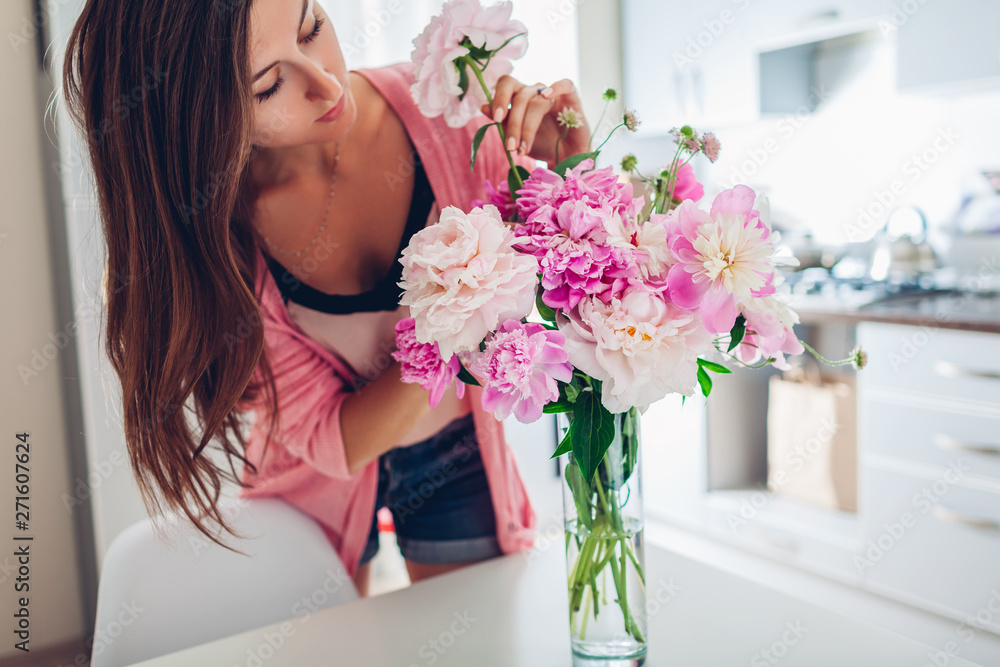 Woman puts peonies flowers in vase. Housewife taking care of coziness and decor on kitchen. Composing bouquet. Woman puts peonies flowers in vase. Housewife taking care of coziness and decor on kitchen. Composing bouquet.