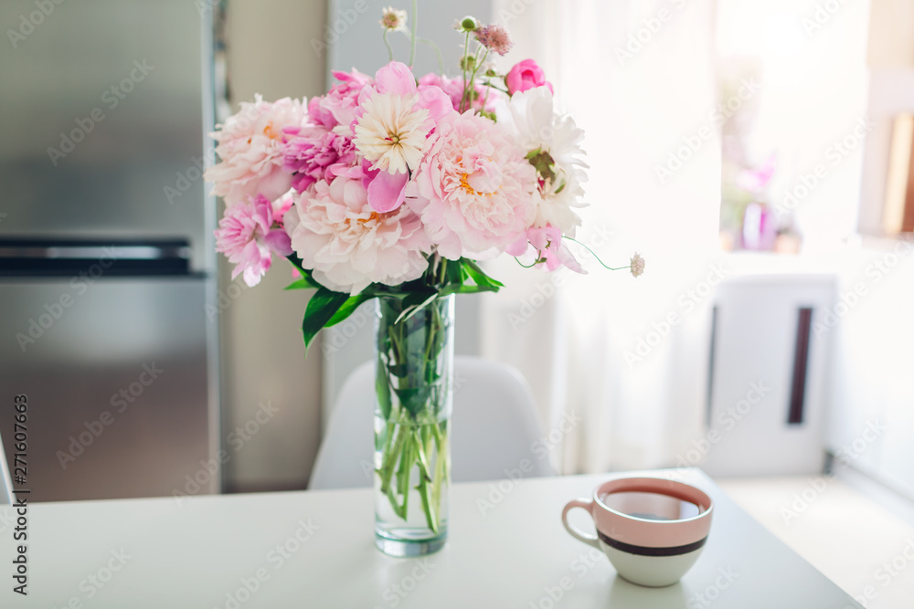Pink peonies with tea on table. Modern kitchen design. Interior of white and silver kitchen decorated with flowers.