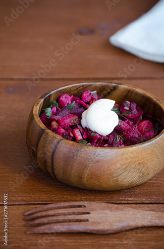 fresh vegetable vegetarian salad with sauce in wooden bowl with wooden fork on wooden table, Russian salad vinaigrette, closeup 45 view