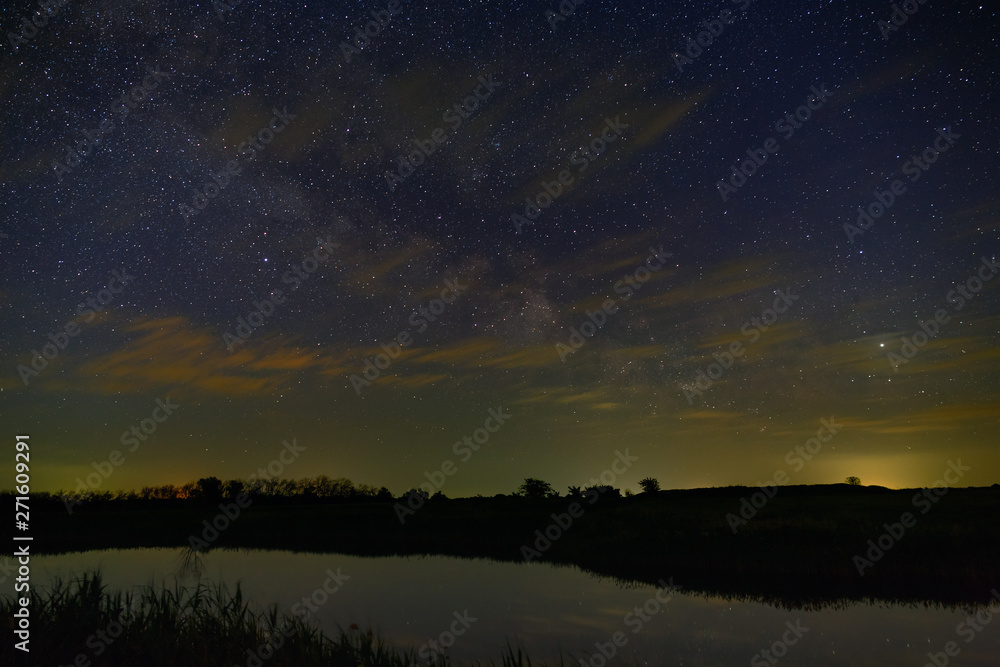 Bright stars with clouds over the river in the night sky. Outer space photographed with long exposure.