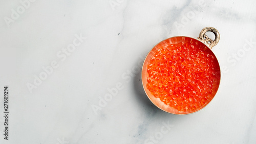 Red caviar top view or flat lay. Bowl of red caviar on white marble background. Copy space for text. Banner photo