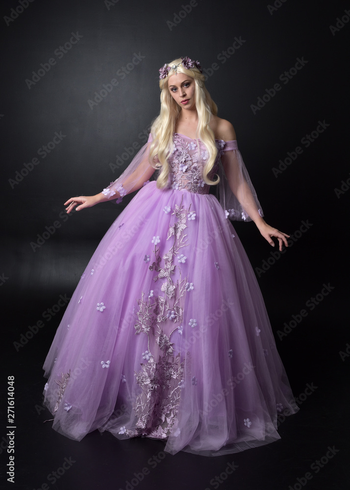 full length portrait of a blonde girl wearing a fantasy fairy inspired costume, long purple ball gown with fairy wings, standing pose on a dark studio background. full length portrait of a blonde girl wearing a fantasy fairy inspired costume, long purple ball gown with fairy wings, standing pose on a dark studio background.