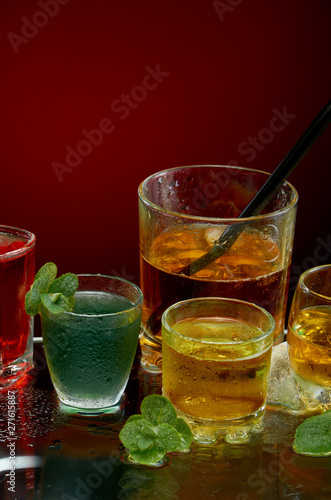 Colored alcoholic drinks with ice and mint on red background