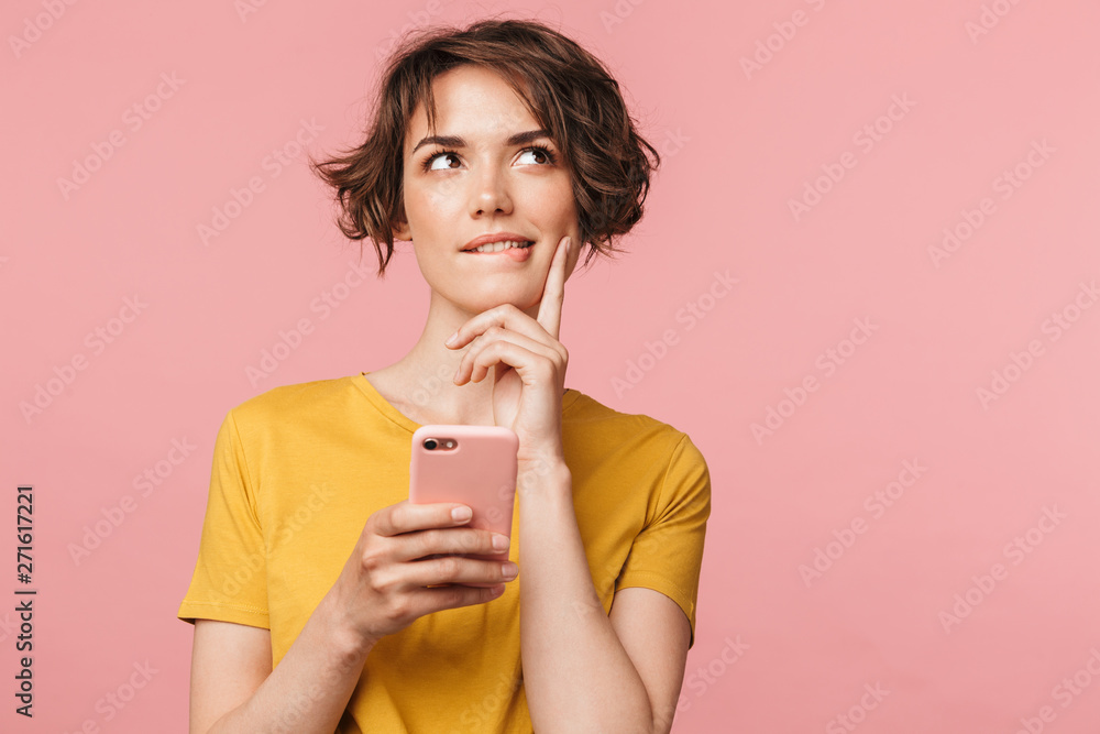 Dreaming young beautiful woman posing isolated over pink wall background using mobile phone. - obrazy, fototapety, plakaty 