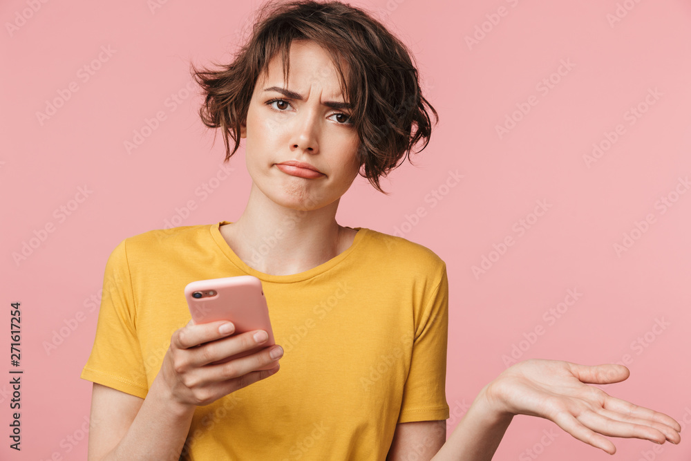 Confused young beautiful woman posing isolated over pink wall background using mobile phone. Confused young beautiful woman posing isolated over pink wall background using mobile phone.