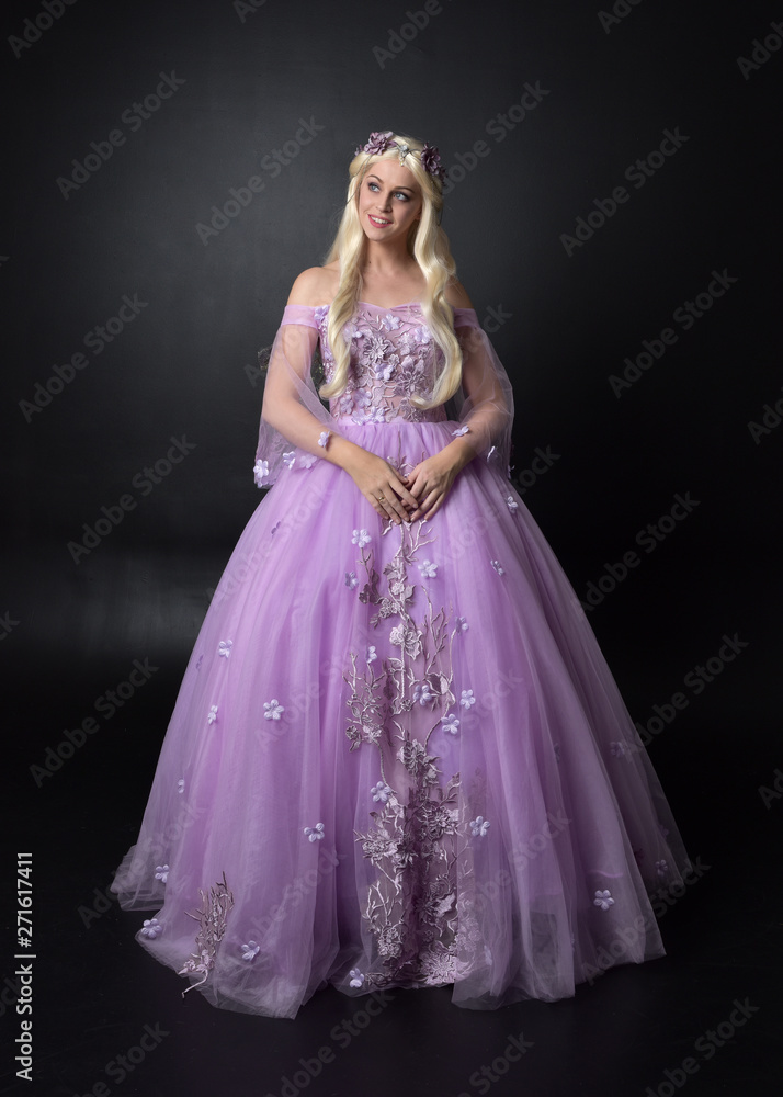 full length portrait of a blonde girl wearing a fantasy fairy inspired costume, long purple ball gown with fairy wings, standing pose on a dark studio background. full length portrait of a blonde girl wearing a fantasy fairy inspired costume, long purple ball gown with fairy wings, standing pose on a dark studio background.